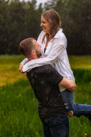 Happy couple embracing in the rain while standing in lush green field.