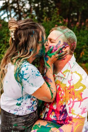 Couple covered in colorful paint playfully embraces during creative outdoor photoshoot.