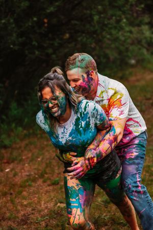 Couple laughs while covered in vibrant paint during outdoor photo session.