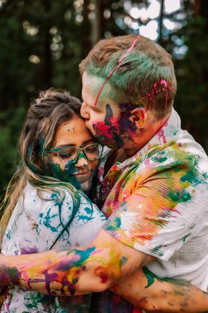 Couple embraces while covered in colorful paint during outdoor photo session.