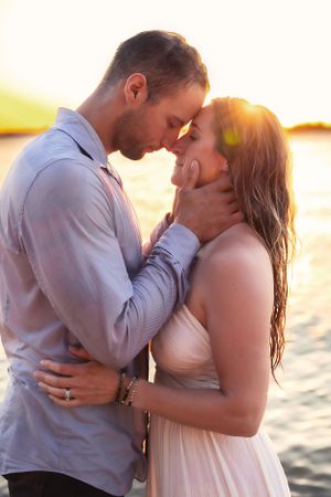 Intimate moment between couple in light colored clothing during sunset by the water.
