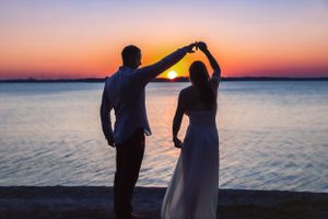 Silhouetted couple dancing against colorful sunset over water.