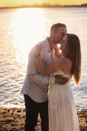 Couple embracing on beach shore during golden hour sunset.