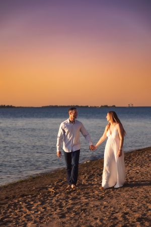 A couple walks hand in hand along a sandy beach during golden hour.