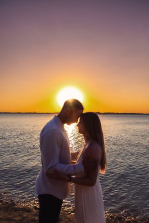 A romantic sunset silhouette of a couple by the water's edge.
