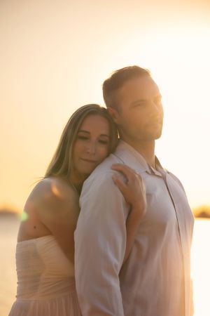 Romantic couple embracing during golden hour sunset by the water in soft light.