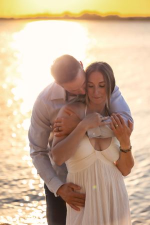 Intimate couple moment on beach at sunset with woman in white dress.