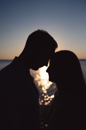 Silhouetted couple in intimate moment against sparkling water at sunset.