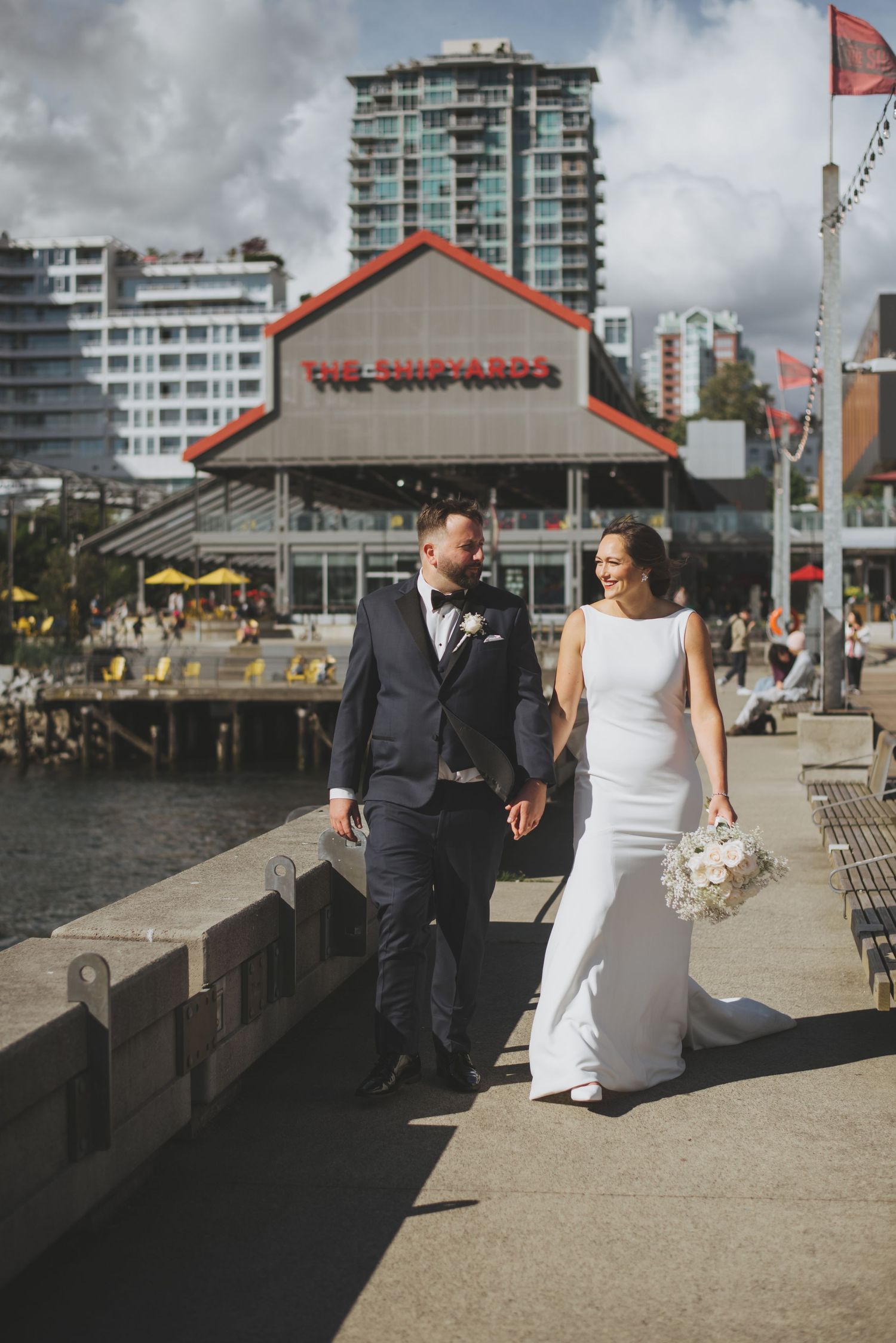 A wedding couple walks along a waterfront promenade near The Keg restaurant.