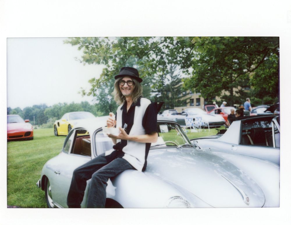 Vintage Porsche and its owner & mechanic sitting on a silver speedster eating lunch. Car show in Ohio. Shot on vintage Polaroid with instax.