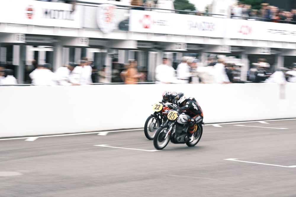 Vintage motorcycles on track at Goodwood Revival by pit lane