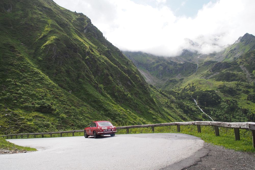 a red MGB GT driving through the alps on a summer day