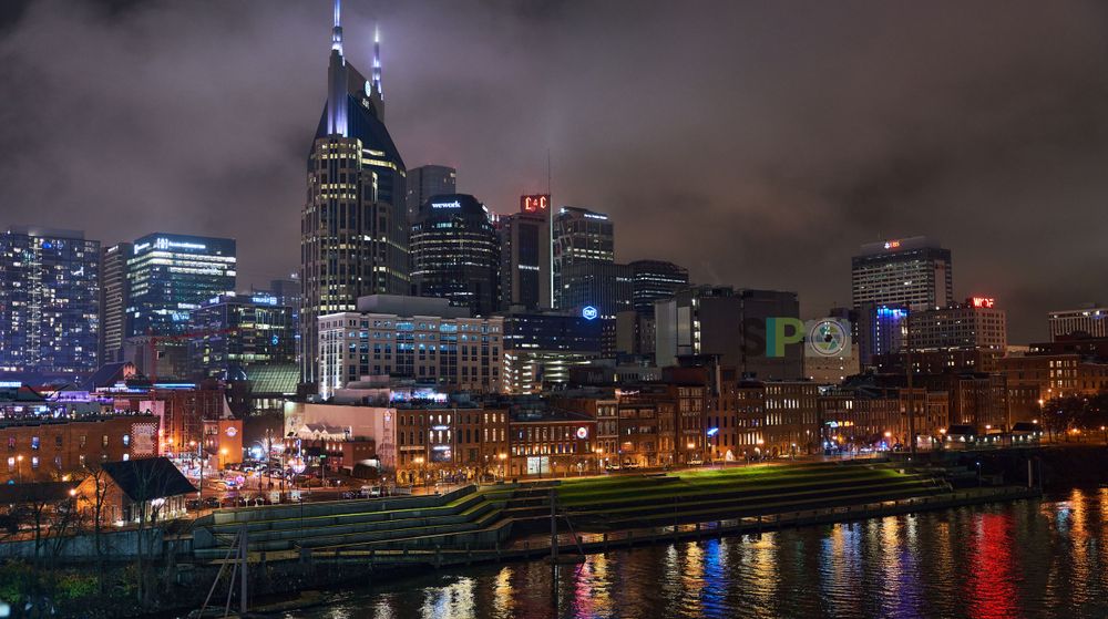 Nashville skyline at night reflecting in Cumberland River with bright city lights.