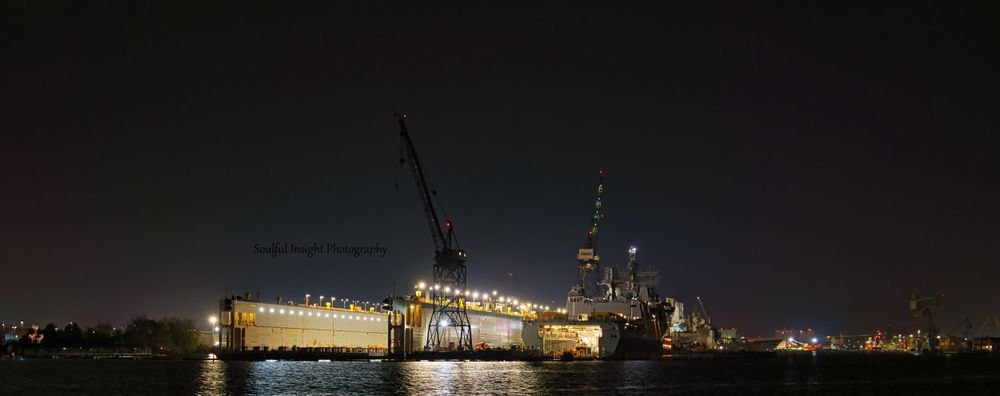 Illuminated ship with cranes at night in an industrial port area.