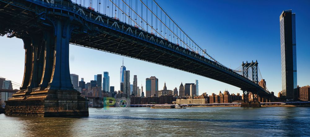 Manhattan Bridge spans East River with New York City skyline in background.
