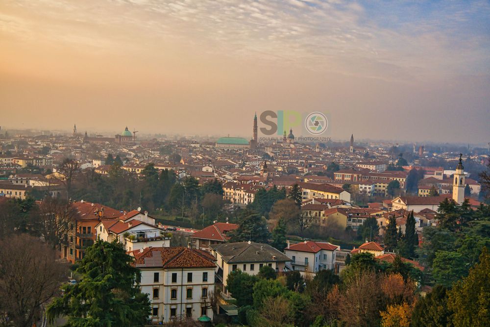 Aerial view of a European city skyline at sunset with orange-tinted rooftops and buildings.