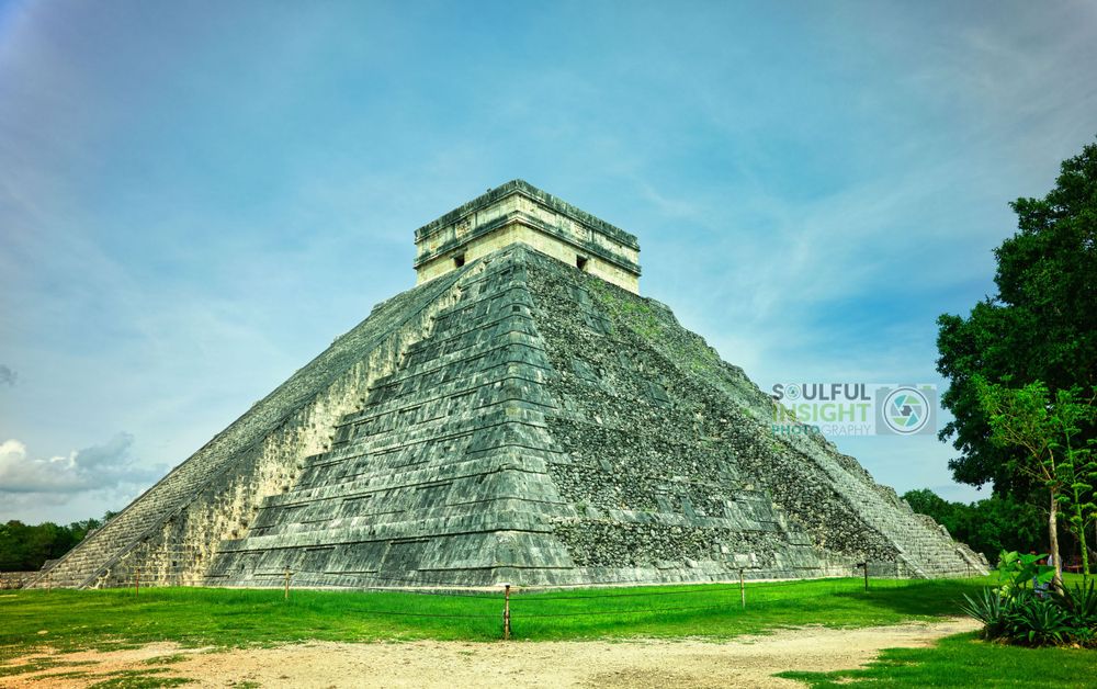 The ancient Mayan pyramid of Chichen Itza stands majestically against a blue sky.
