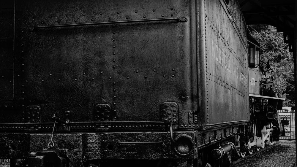 Side view of vintage train car in black and white showing industrial details and rivets.