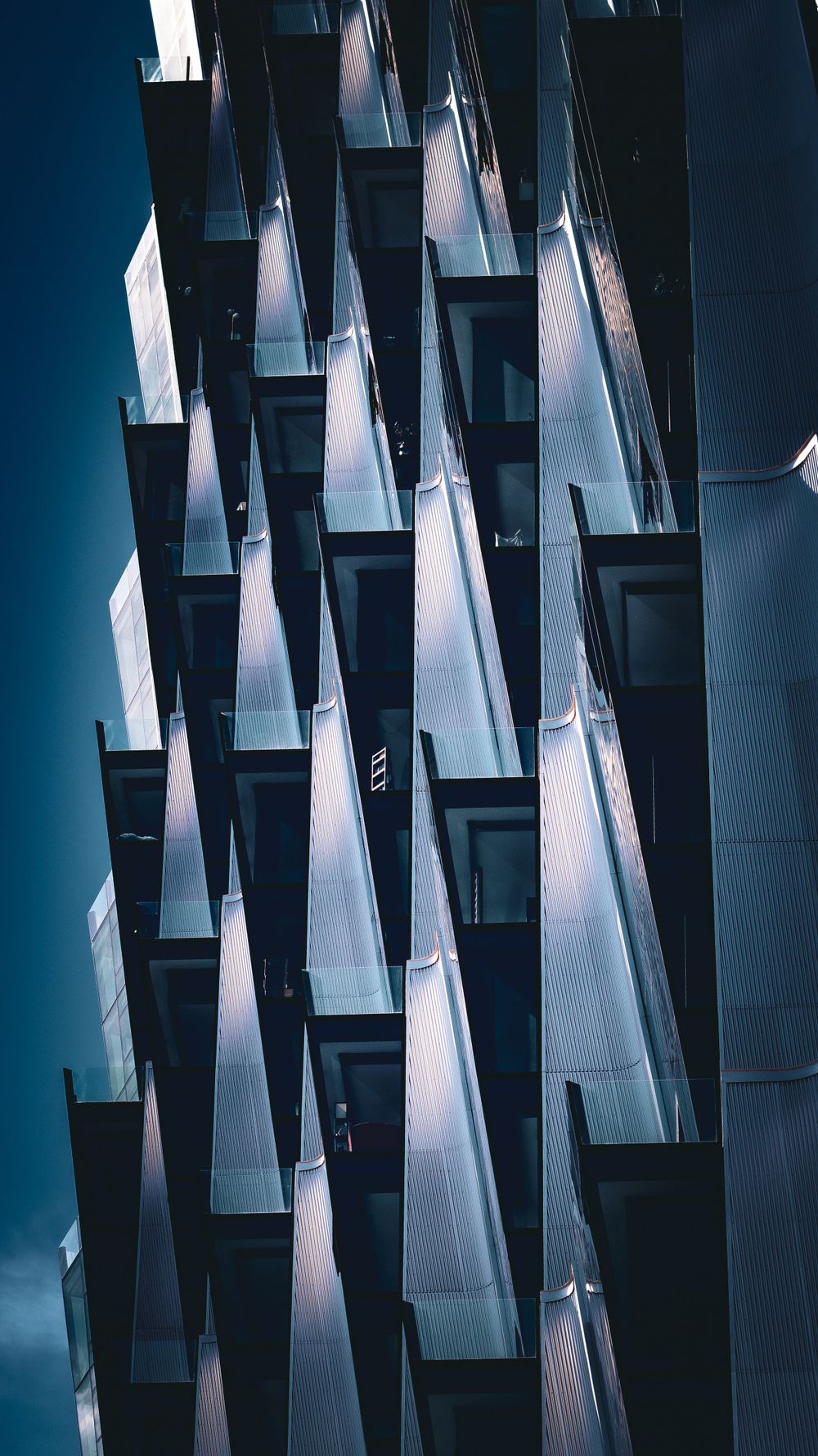 Modern architectural detail of angular balconies creating geometric patterns against a deep blue sky.