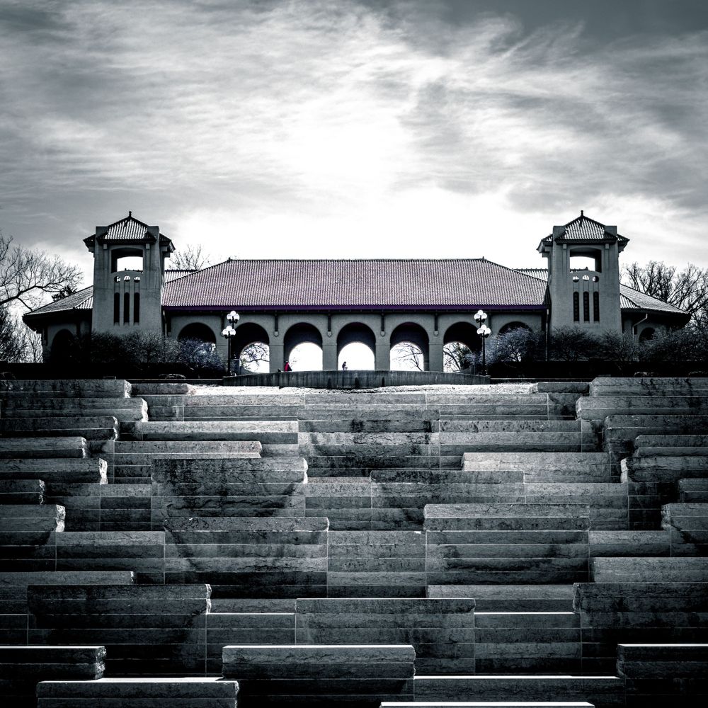 Historic amphitheater with stone steps and arched colonnade photographed in dramatic black and white.