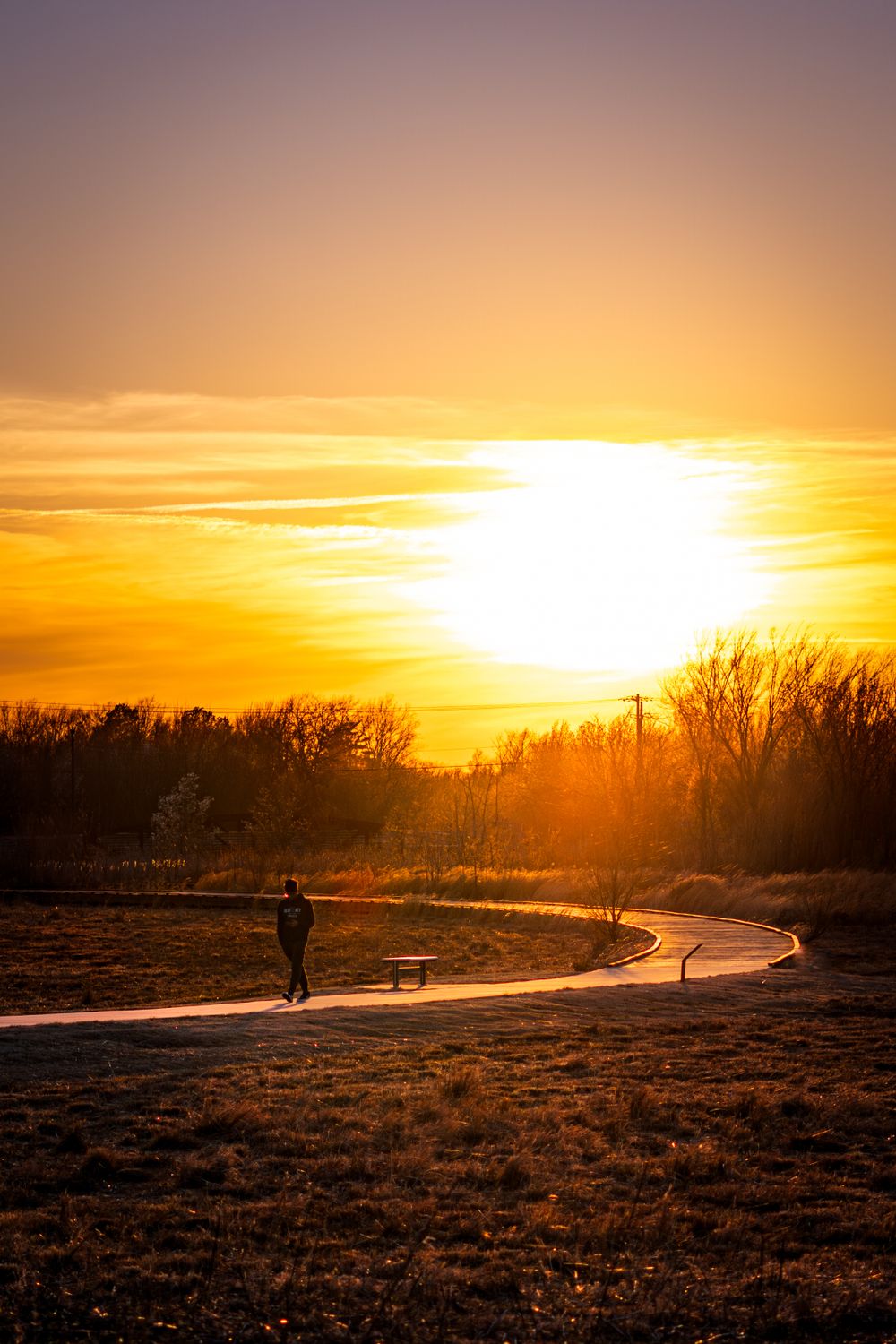 Silhouette of a person walking on a path during golden sunset with dramatic orange sky.