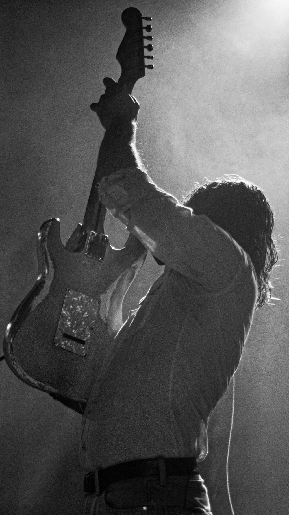 Dramatic silhouette of a musician holding up an electric guitar in black and white.