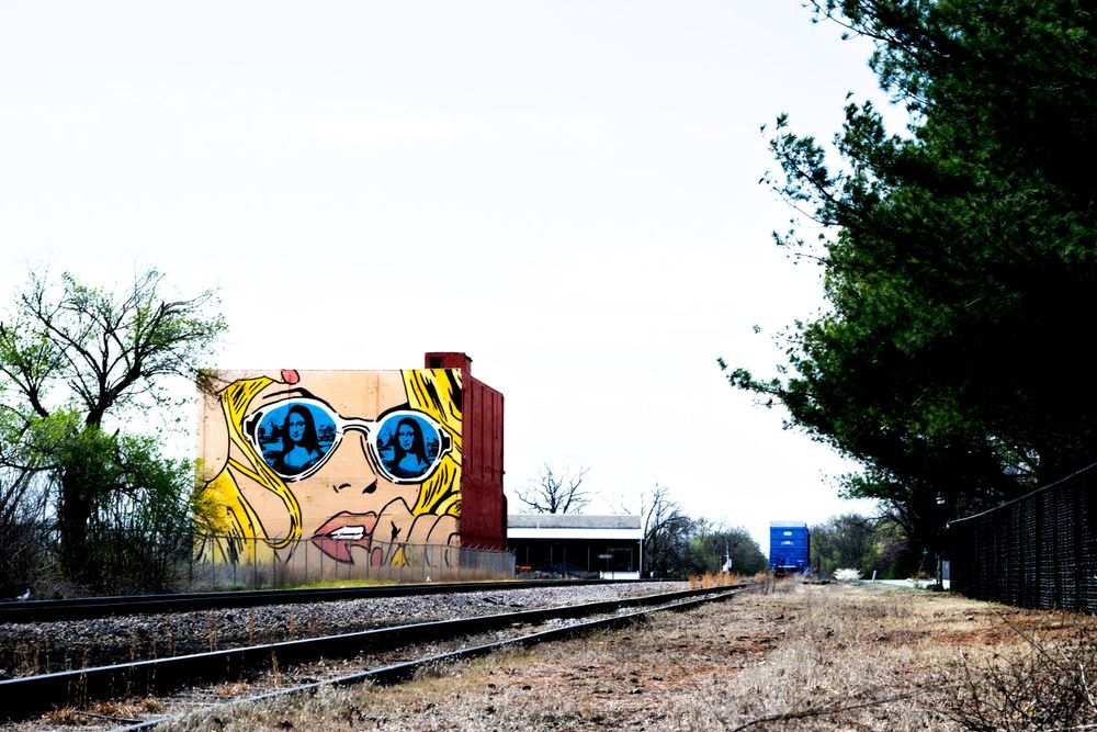 Colorful street art featuring sunglasses decorates an abandoned railway car along train tracks.