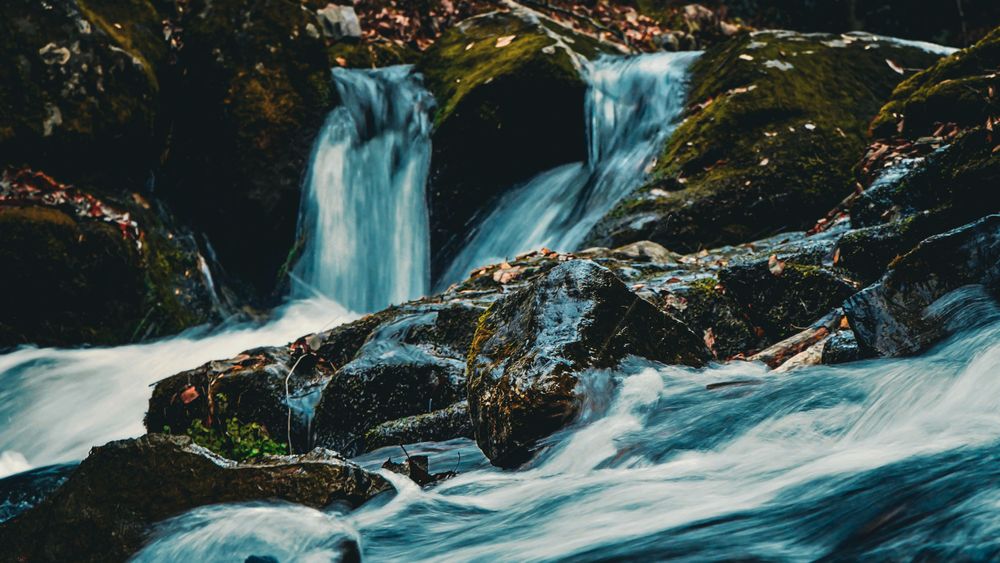 Cascading waterfall flows over moss-covered rocks with long exposure creating smooth water effect.