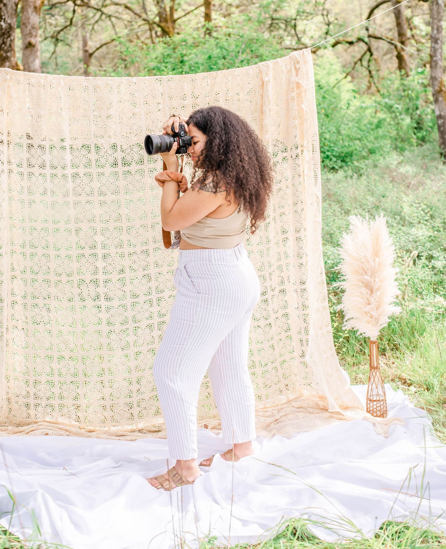 Ethereal picnic setup with white linens and macrame backdrop in a sunny forest clearing.