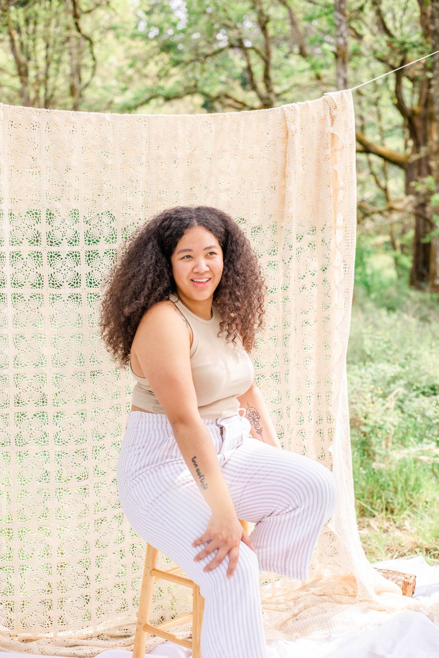 Casual portrait session with boho-inspired white lace backdrop and rustic stool in woodland setting.