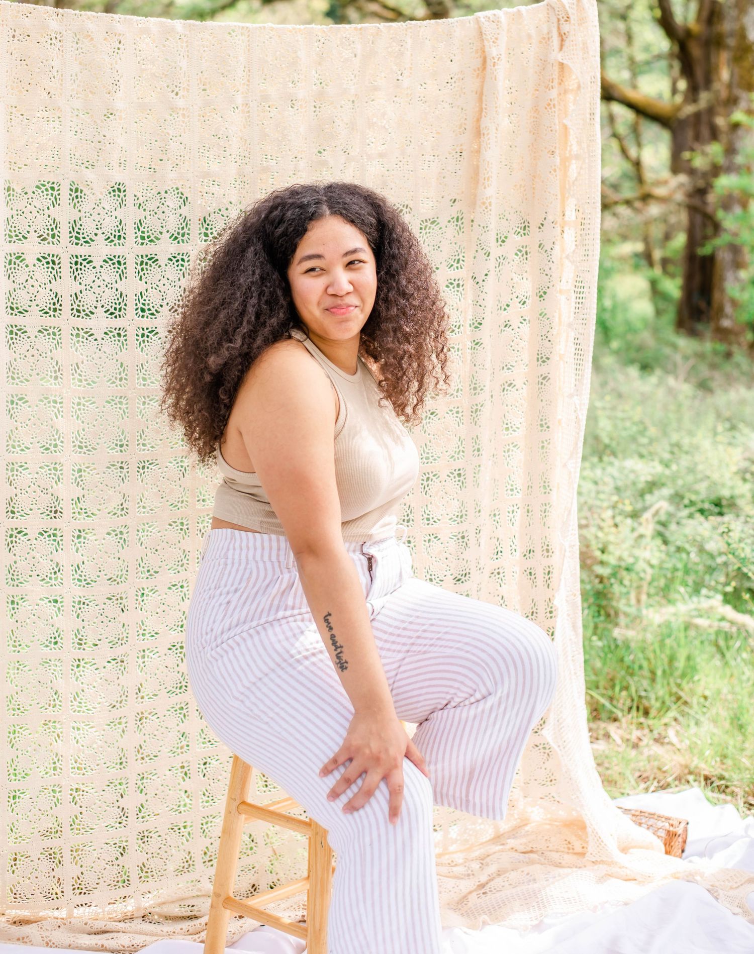 Artistic outdoor photo setup with cream macrame backdrop and wooden stool on white fabric.