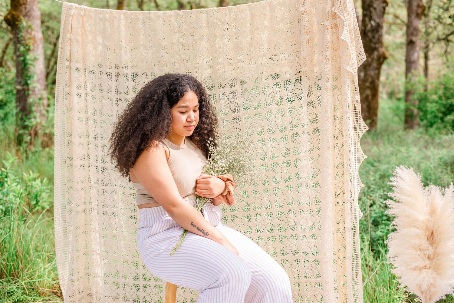 Bohemian outdoor photo scene with macrame backdrop and rustic stool against green forest.