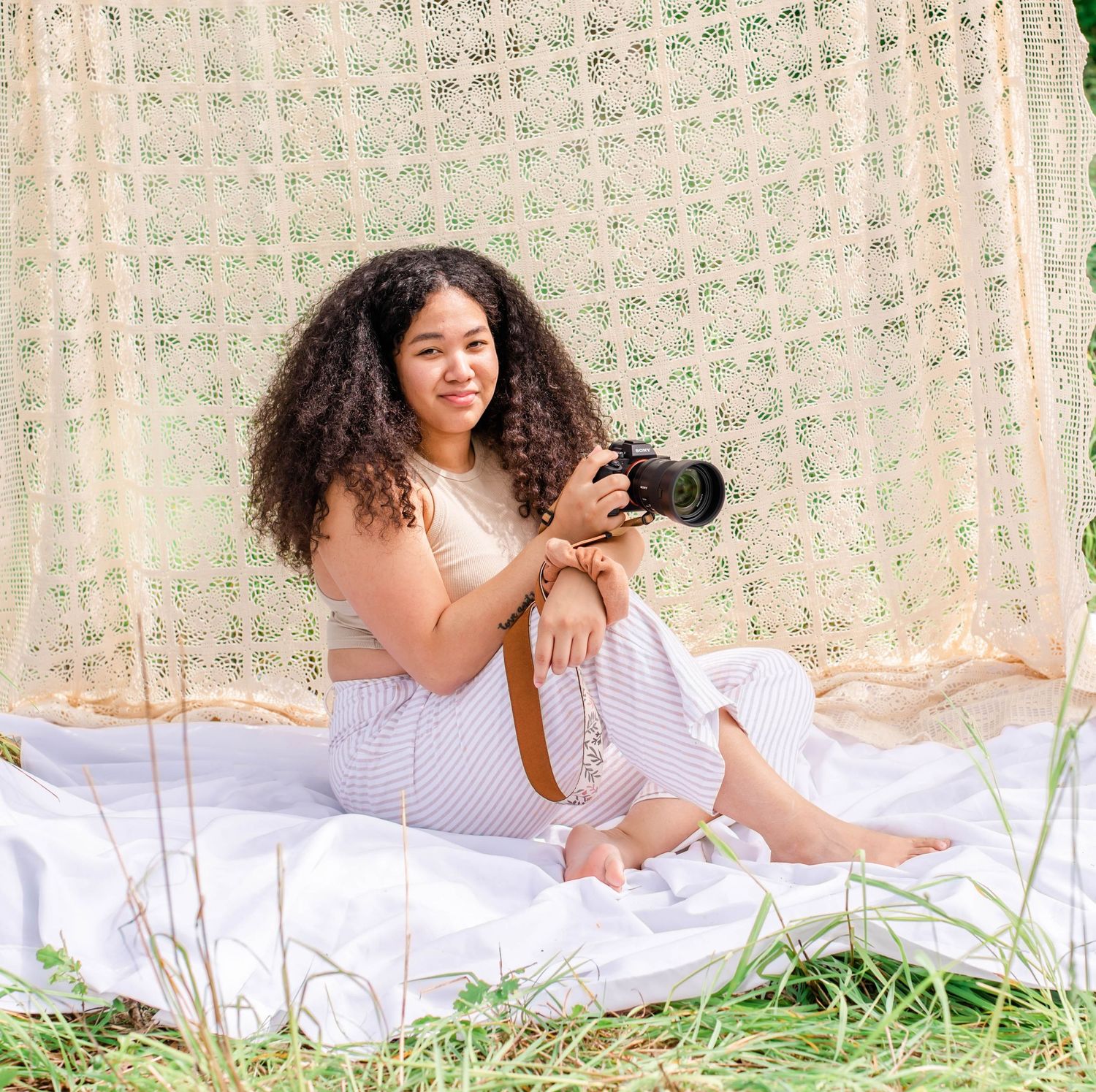 Person in white dress poses with camera on blanket during outdoor photography session.