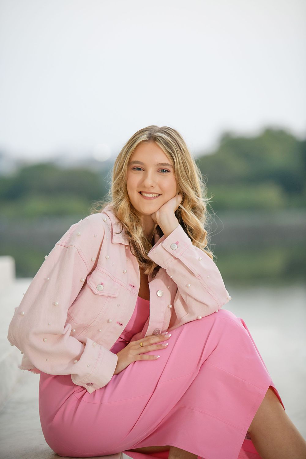 Portrait in pink attire by waterfront with soft natural lighting.