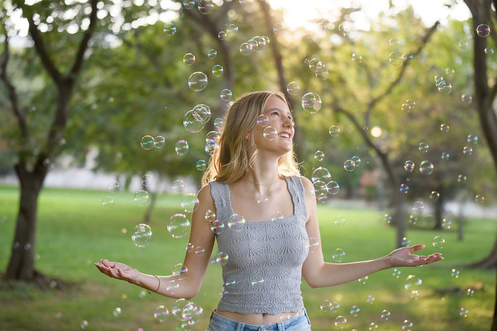 Playful outdoor portrait with floating bubbles in summer park setting.