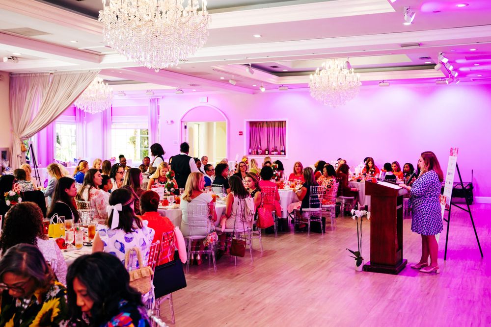 Elegant banquet hall event with pink lighting, crystal chandeliers, and guests seated at round tables.