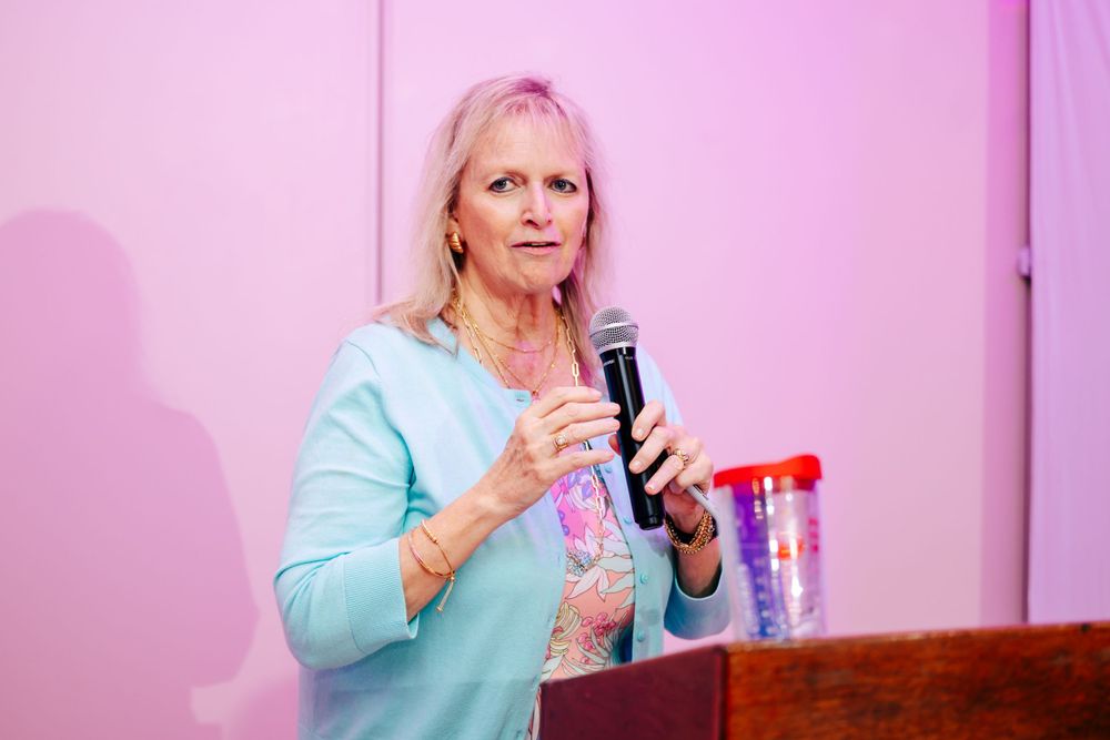 Speaker presenting in light blue attire against pink backdrop at women's foundation event.