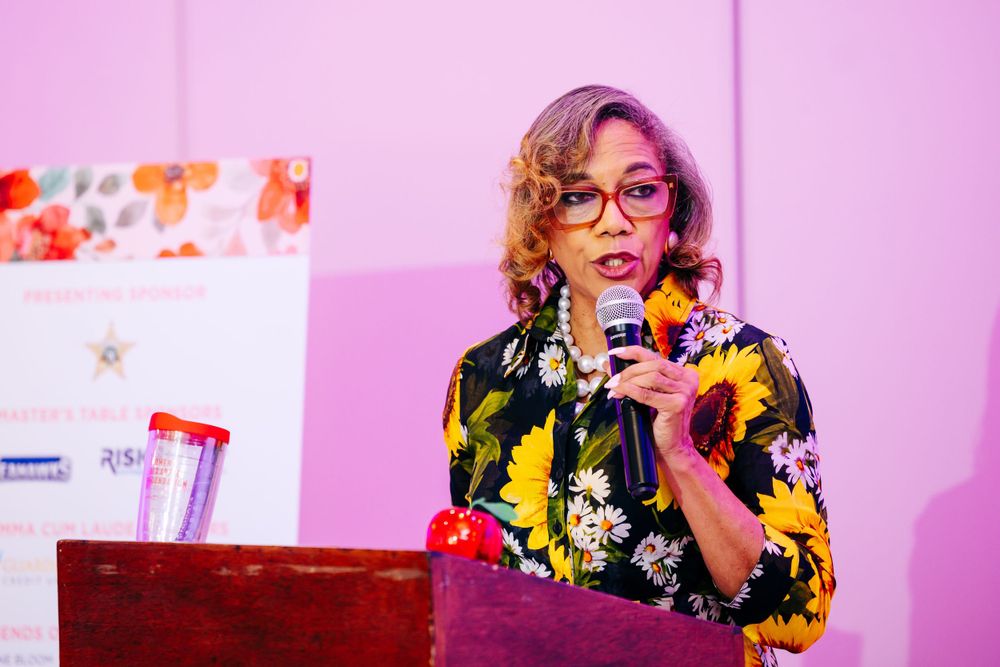 Speaker engaging with audience from podium at Women's Red Apple Foundation gathering.