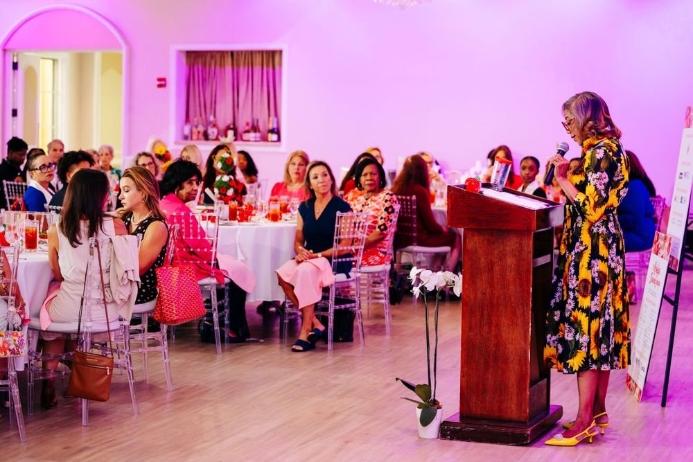 Wide view of audience seated at tables during Women's Red Apple Foundation event.