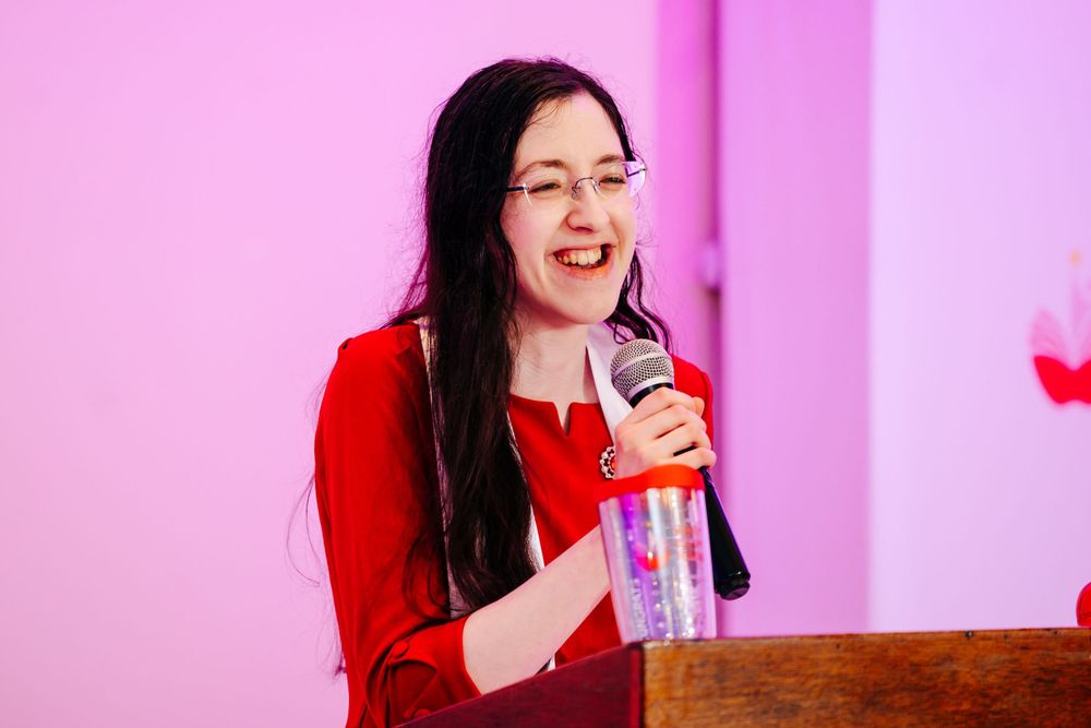 Speaker engages audience with microphone at pink-lit corporate function or celebration.