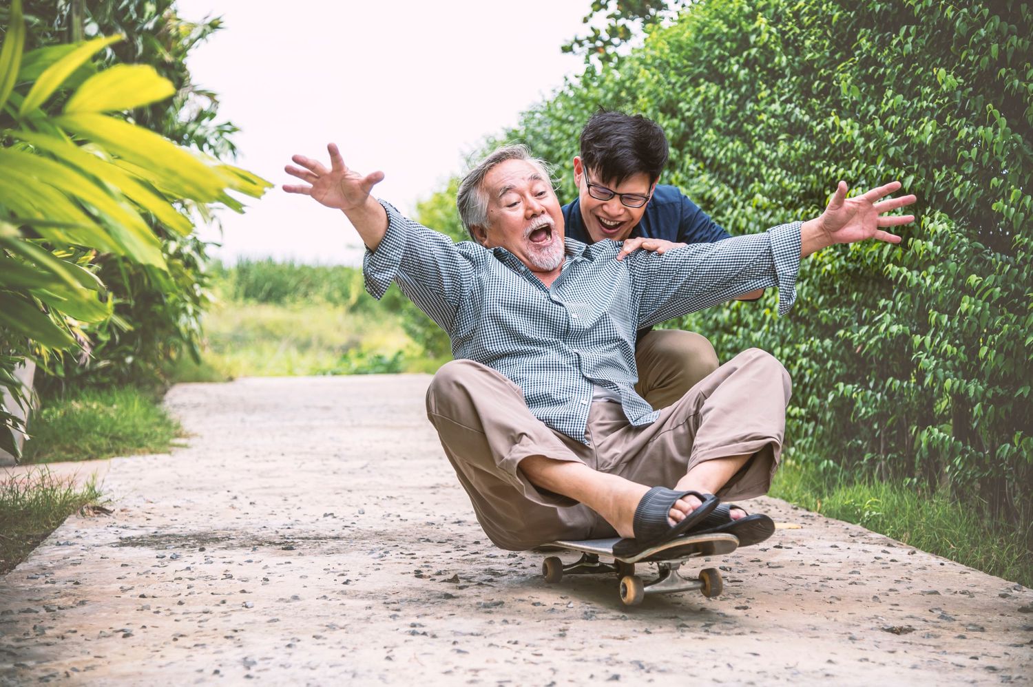 grandfather sits joyfully on a skateboard as his grandson pushes him happy to have the best insurance