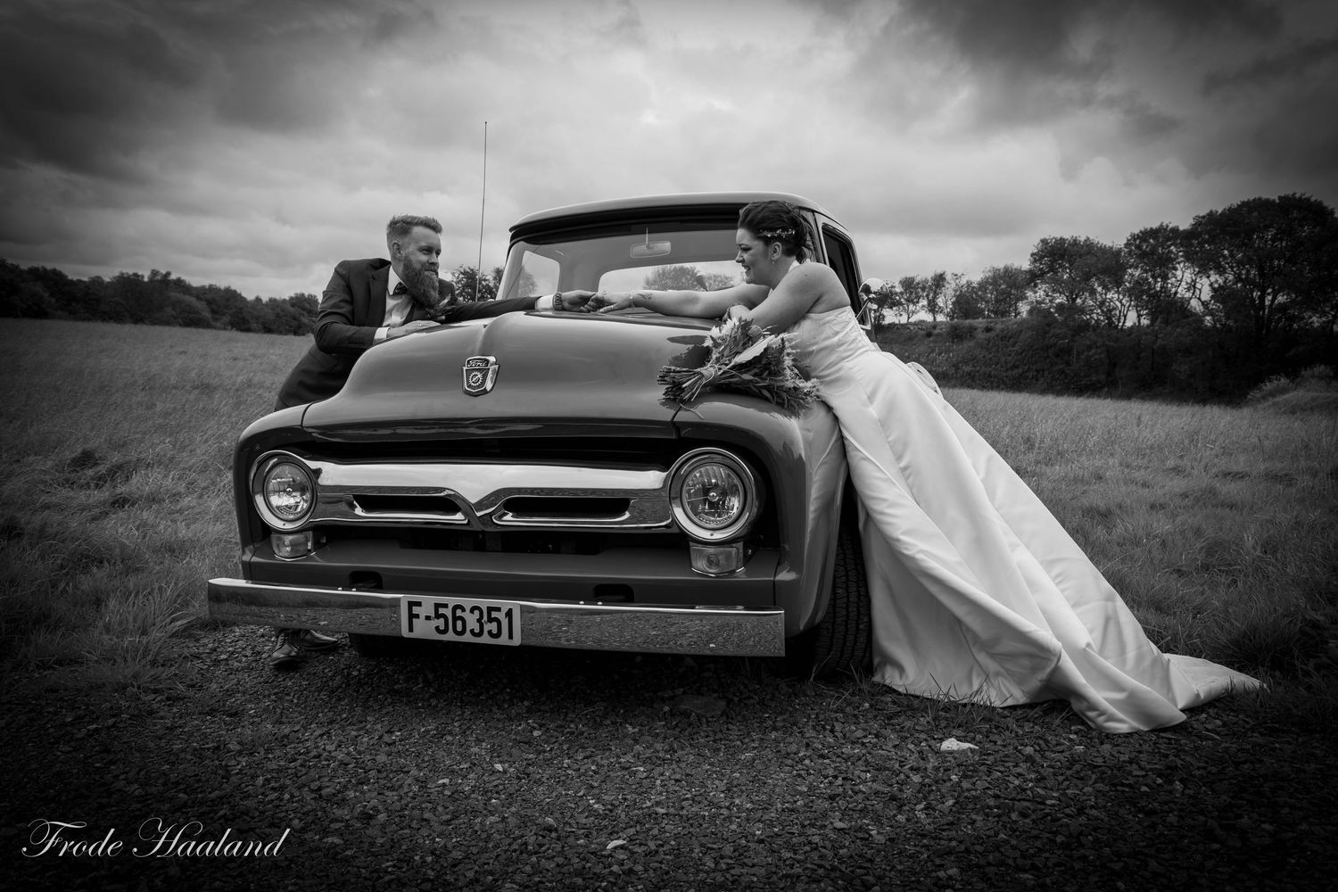 Bride and groom posing with vintage Ford truck in black and white outdoor wedding photo.