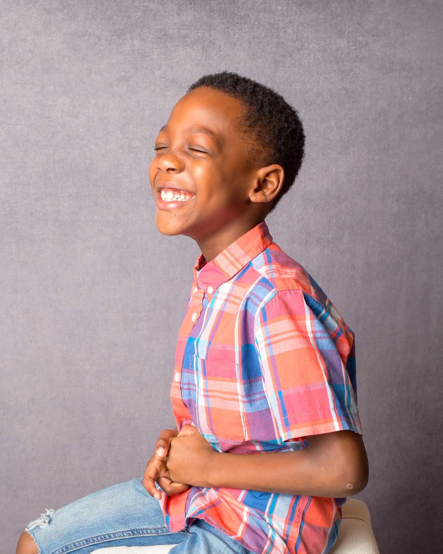 Young boy in plaid shirt laughing joyfully during studio portrait session.