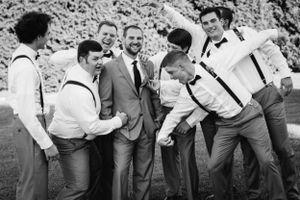 Groomsmen in suspenders having fun and laughing together outdoors.
