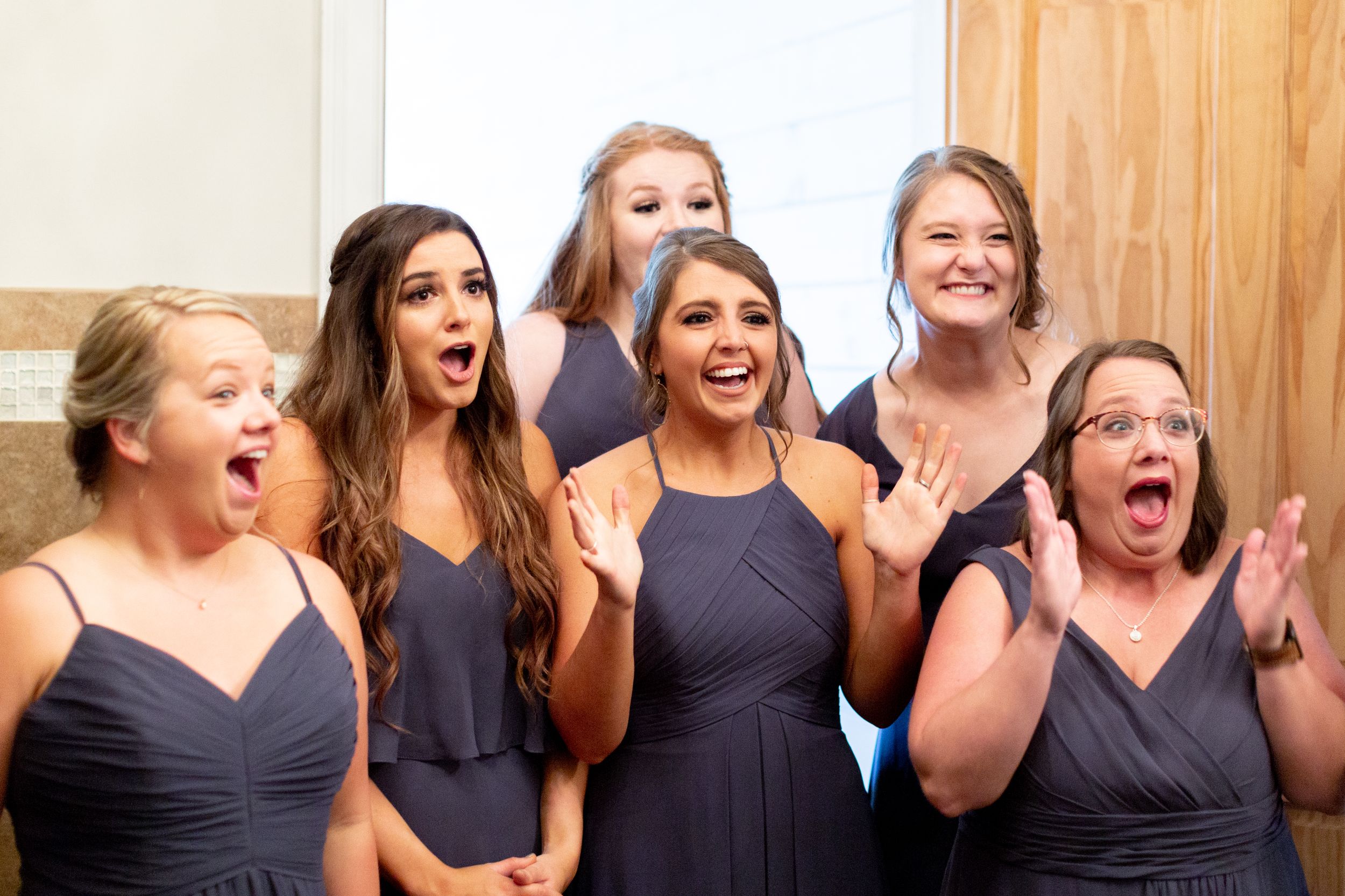 Bridesmaids in navy dresses react with excitement during wedding festivities.