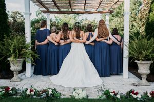 Wedding party lined up showing backs with bridesmaids in navy dresses and bride in white gown.