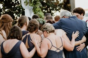 Group wearing navy dresses huddle together in emotional embrace.