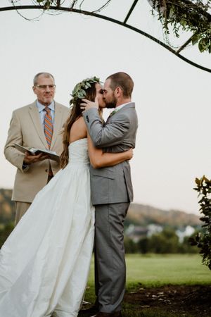 Intimate wedding ceremony moment under natural vine arch at outdoor venue.