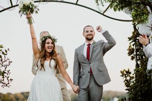 Newlyweds celebrate joyfully under a floral arch during an outdoor wedding ceremony.