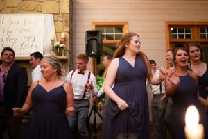 Wedding guests in purple dresses dance and celebrate at an indoor reception.